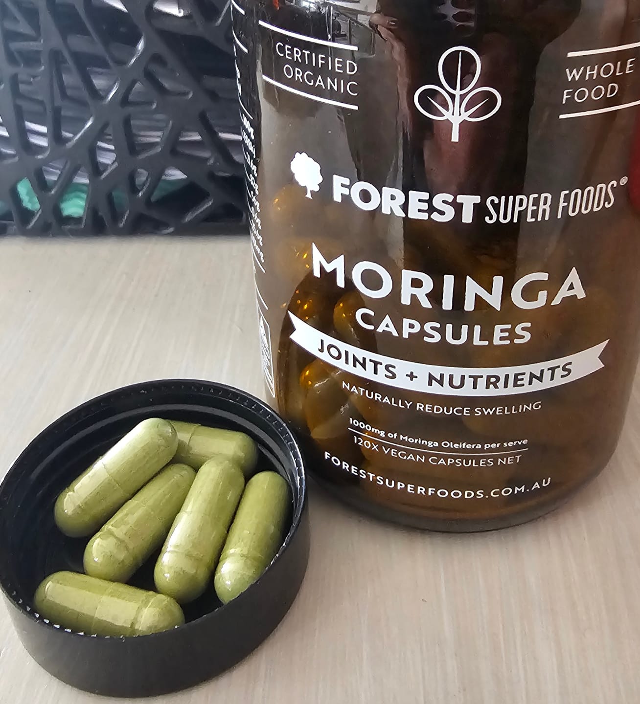 Organic Moringa Capsules Close Up Open bottle of Forest Super Foods Organic Moringa Capsules showing green whole-leaf moringa capsules.